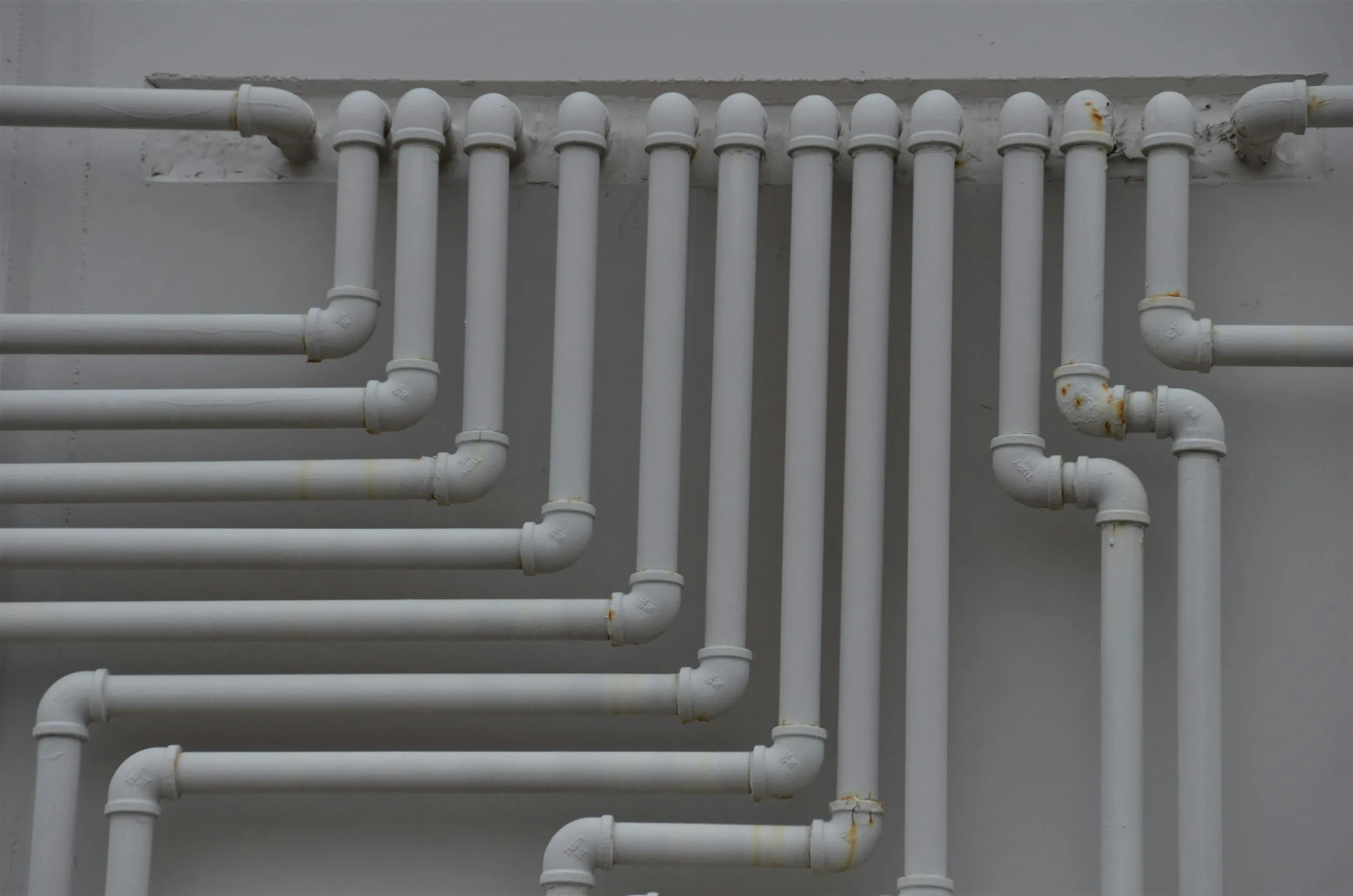 Grey rigid PVC pipe runs and fittings arranged against a wall